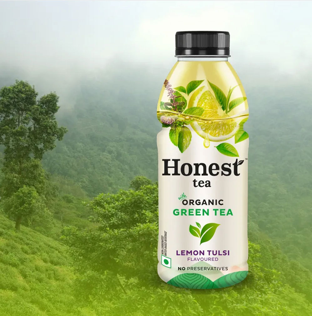 Bottle of Honest organic green tea with lemon tulsi flavor, forest background.