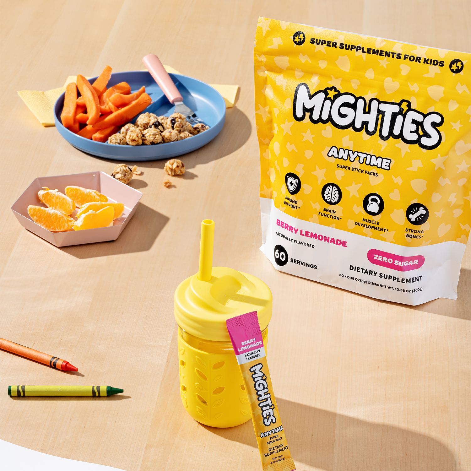 Kids supplement packaging with snacks, a drink bottle, crayons, and sliced oranges on a table.