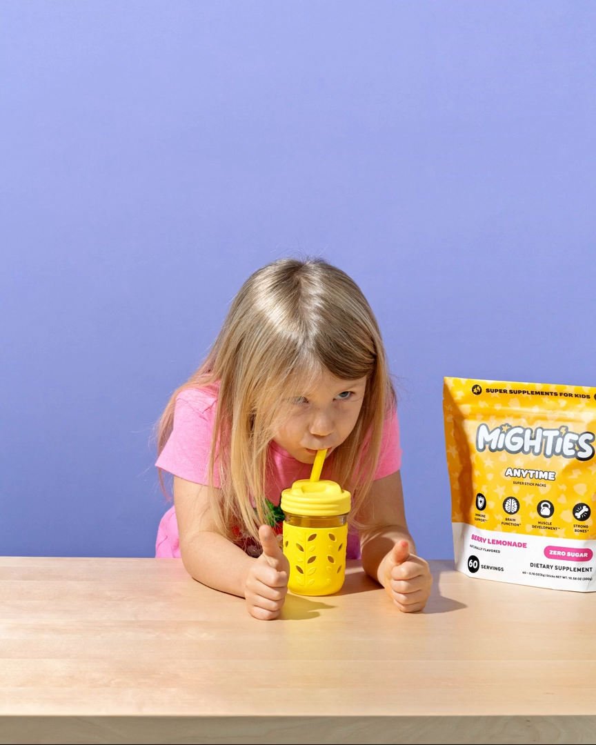 Child drinking from a yellow cup with a packet of supplements on the table.