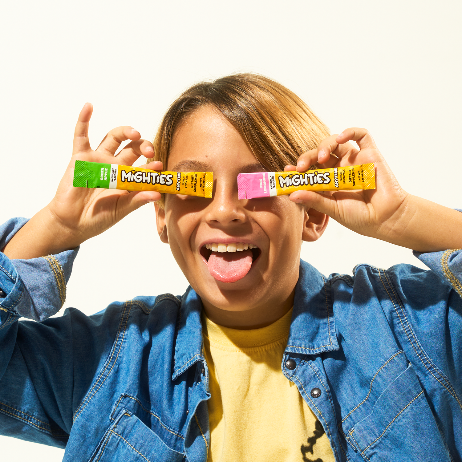 Child holding candy wrappers over eyes, sticking tongue out, wearing a blue jacket.