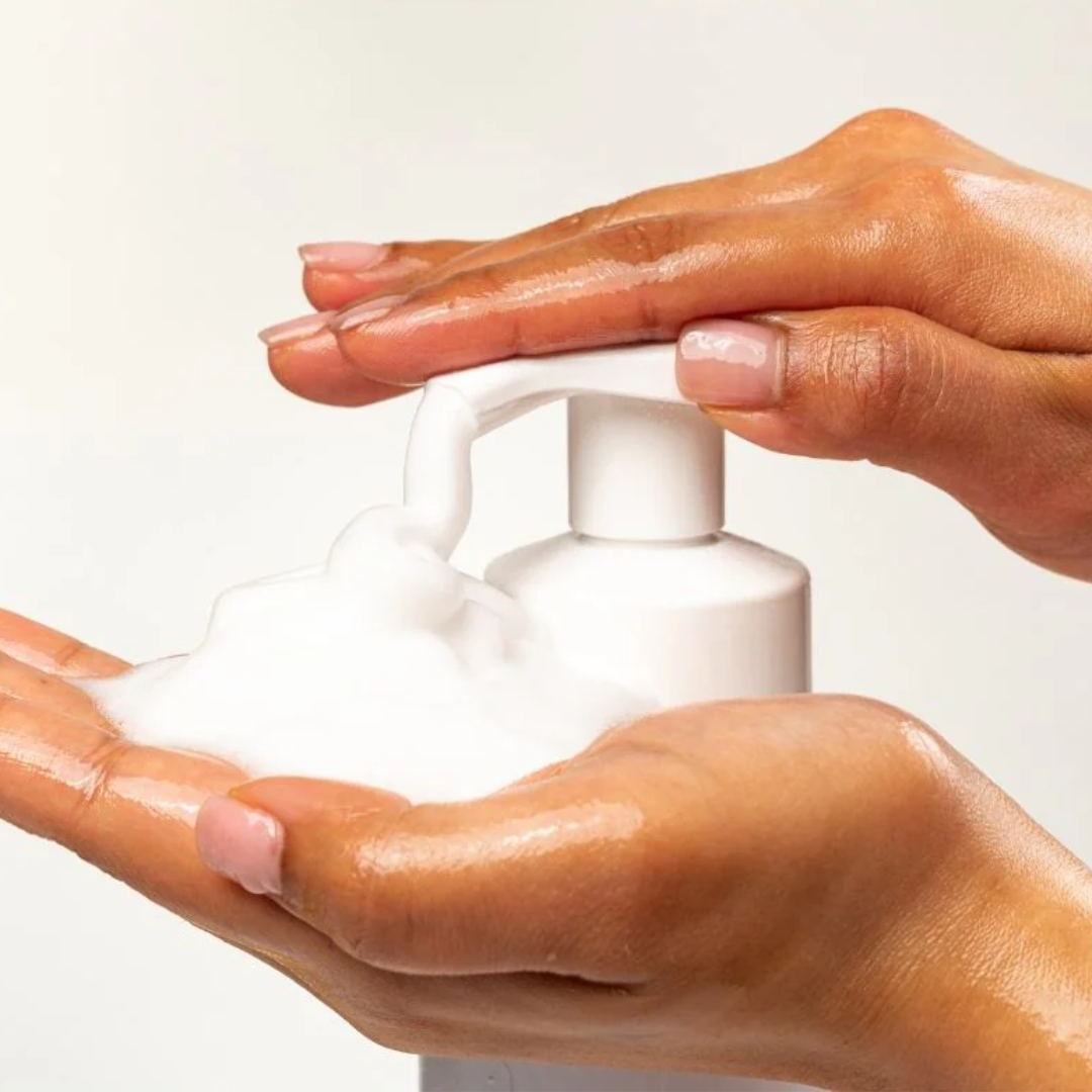 Green foaming hand wash bottle with small colorful bottles on a marble tray.