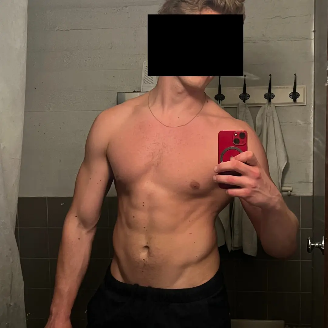 Shirtless person taking a mirror selfie in a bathroom.