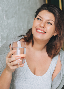 Smiling person holding a glass of water indoors.