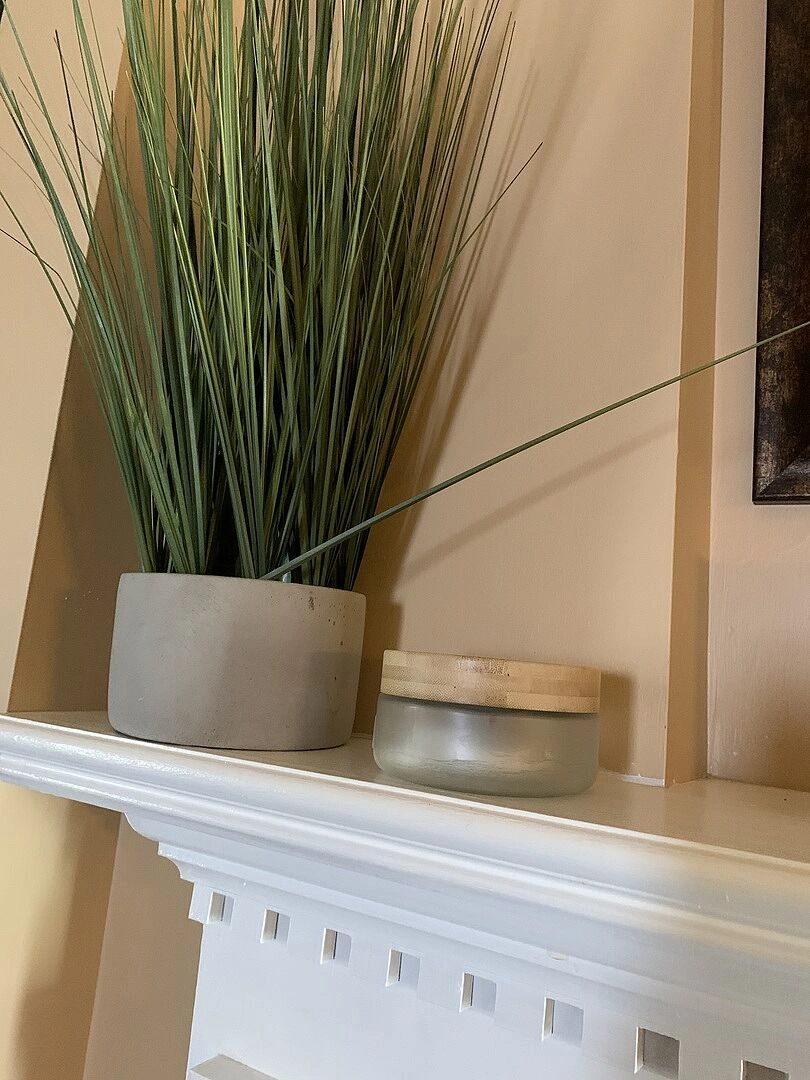 Tall grass plant and a frosted jar on a white mantel.