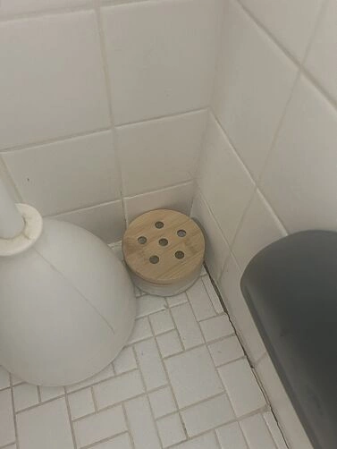 Wooden object with holes on tiled bathroom floor near a toilet brush.