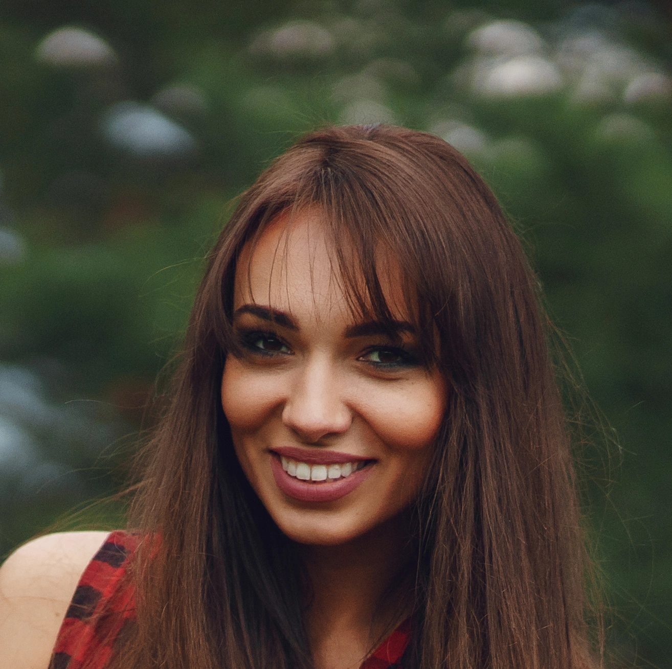 Woman smiling outdoors with blurred green background.