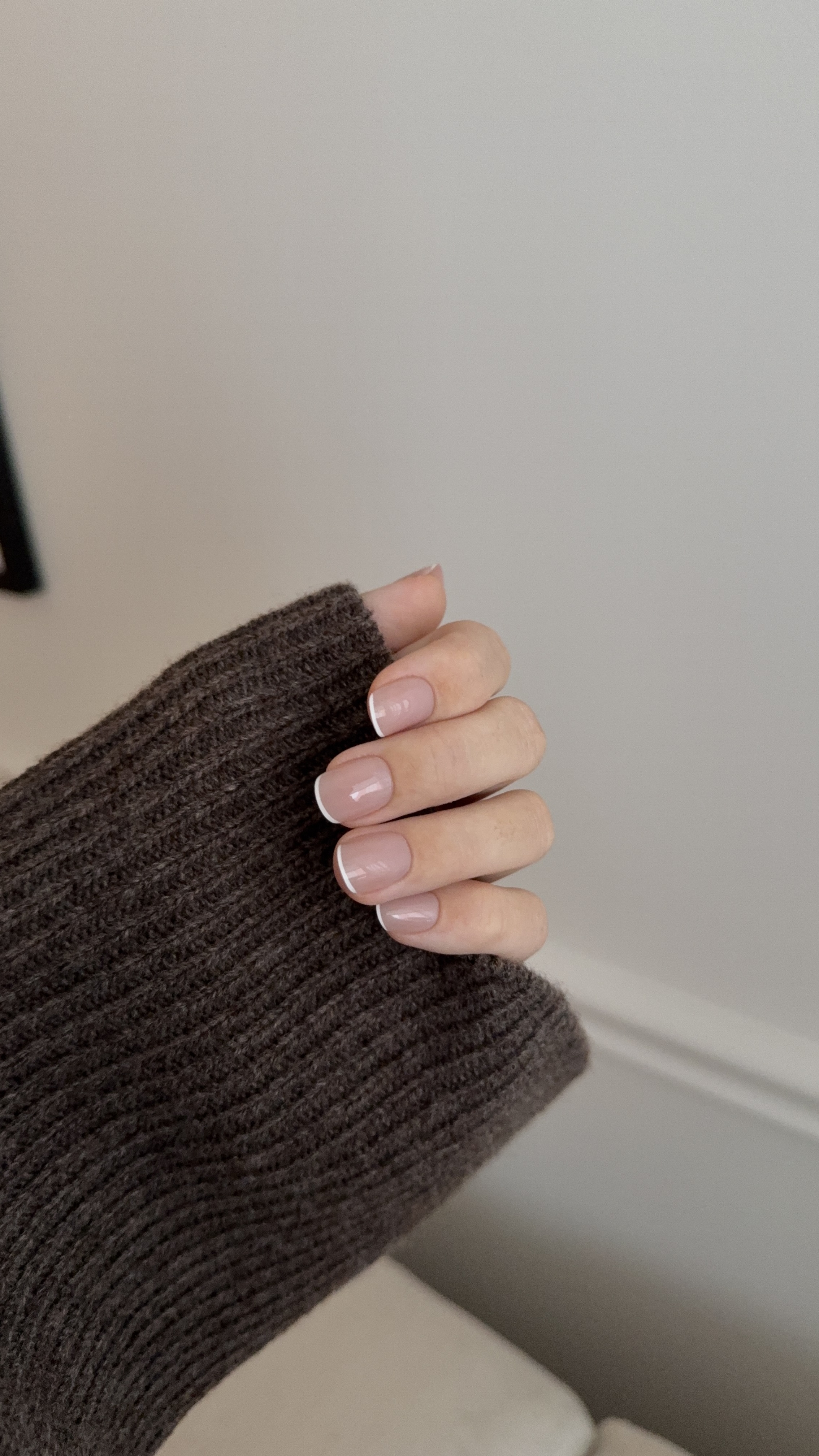 Hand with French manicure in a brown sweater sleeve.