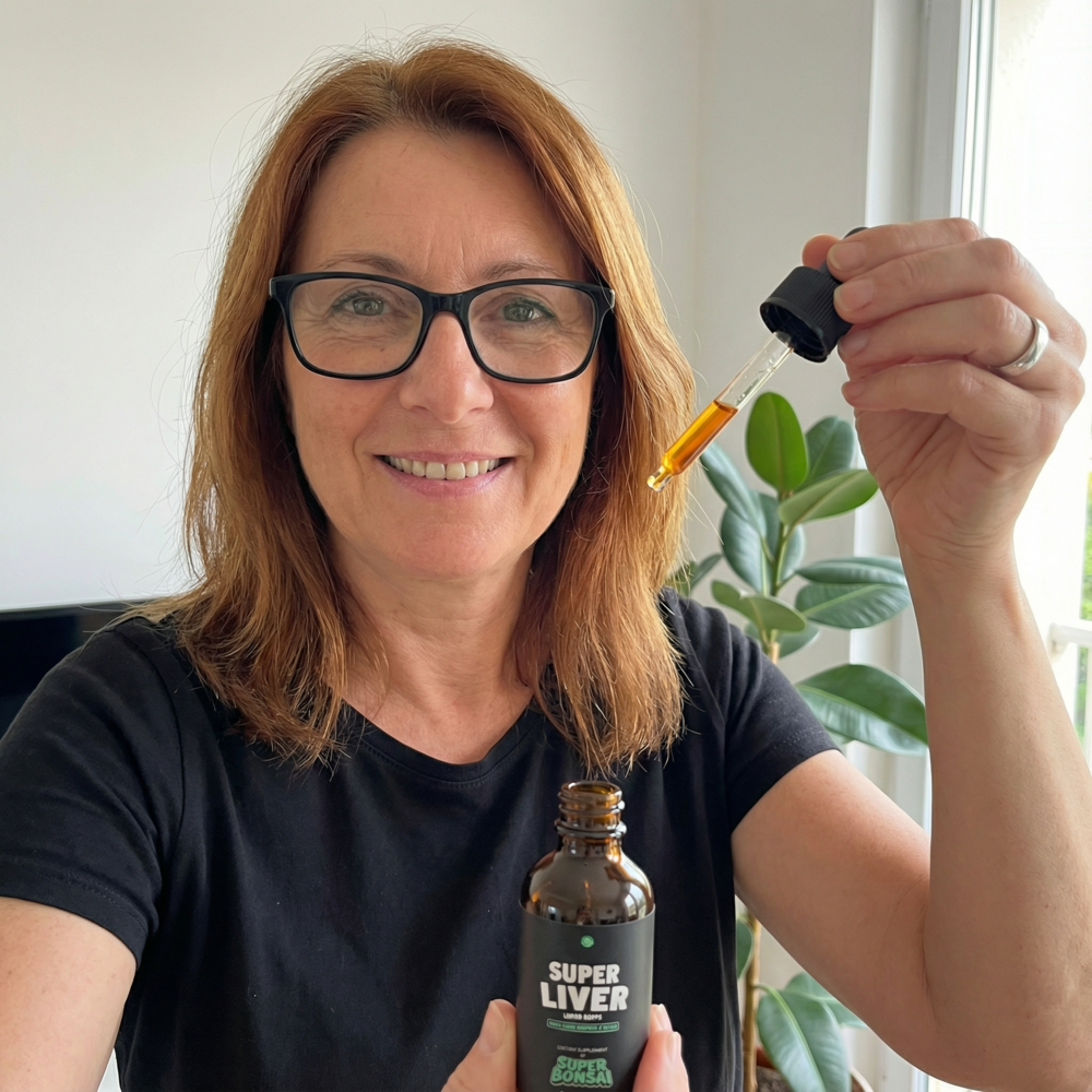 A smiling woman in glasses holds a bottle of Super Liver liquid drops and a filled dropper.