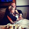 A couple hugging closely in a cozy indoor setting, with tableware visible in the foreground.