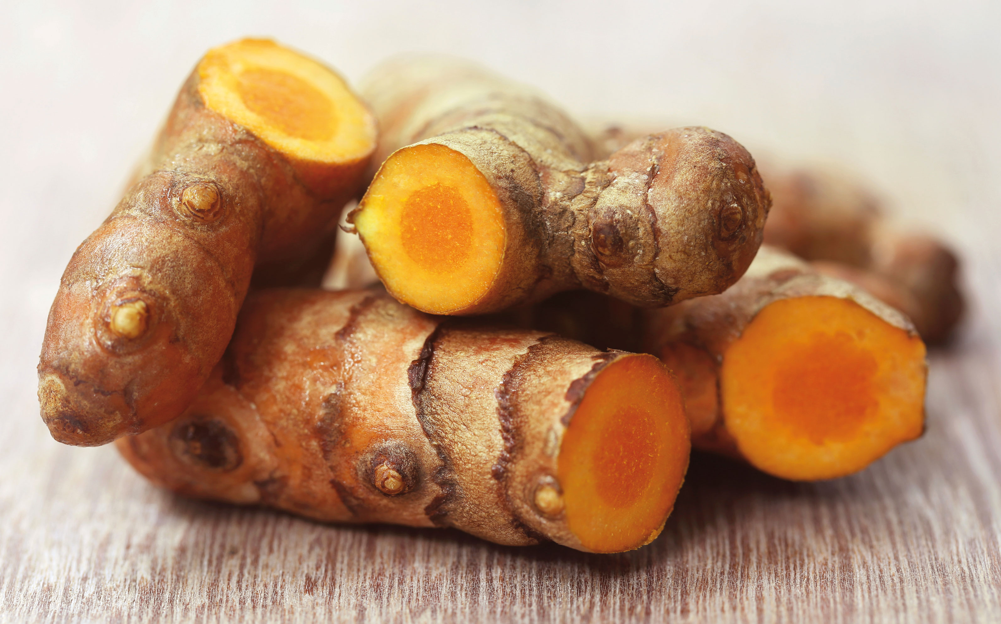 A close-up of fresh turmeric root, with some pieces sliced to show their vibrant orange interior.