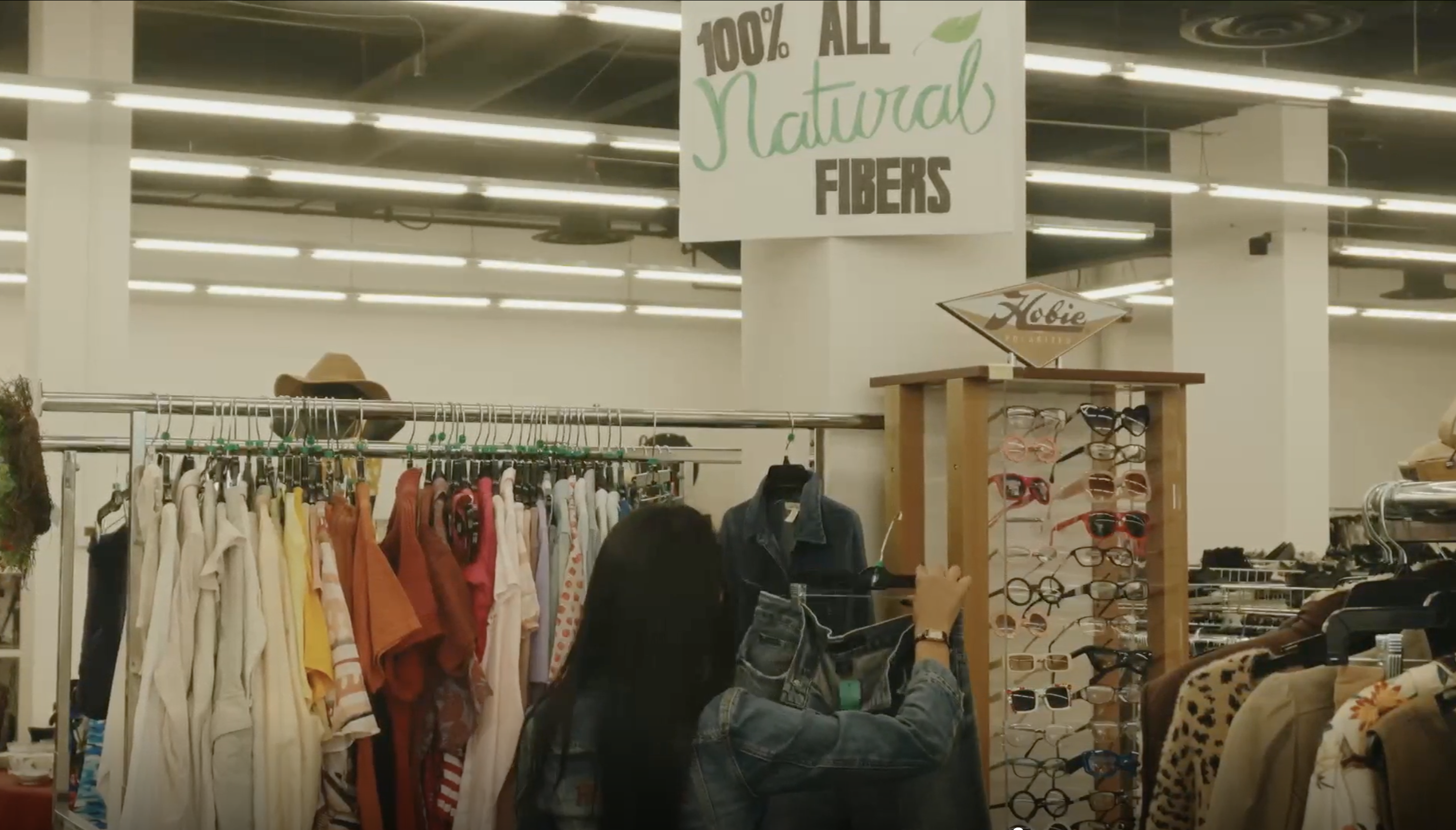 People browse racks of second-hand clothing and a sunglasses display in a store.