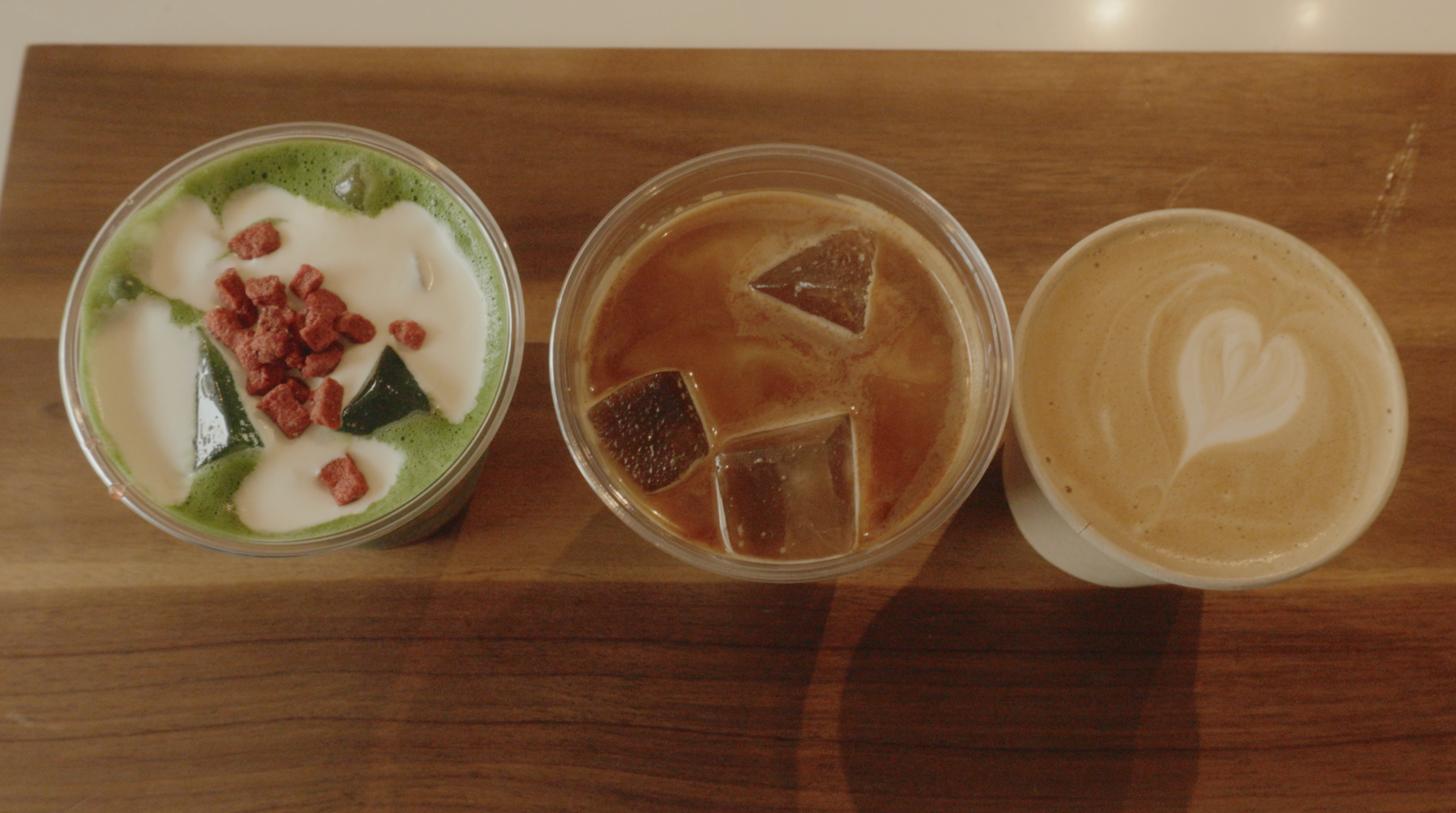 An overhead view of three coffee drinks in a row: an iced matcha, an iced coffee, and a latte.