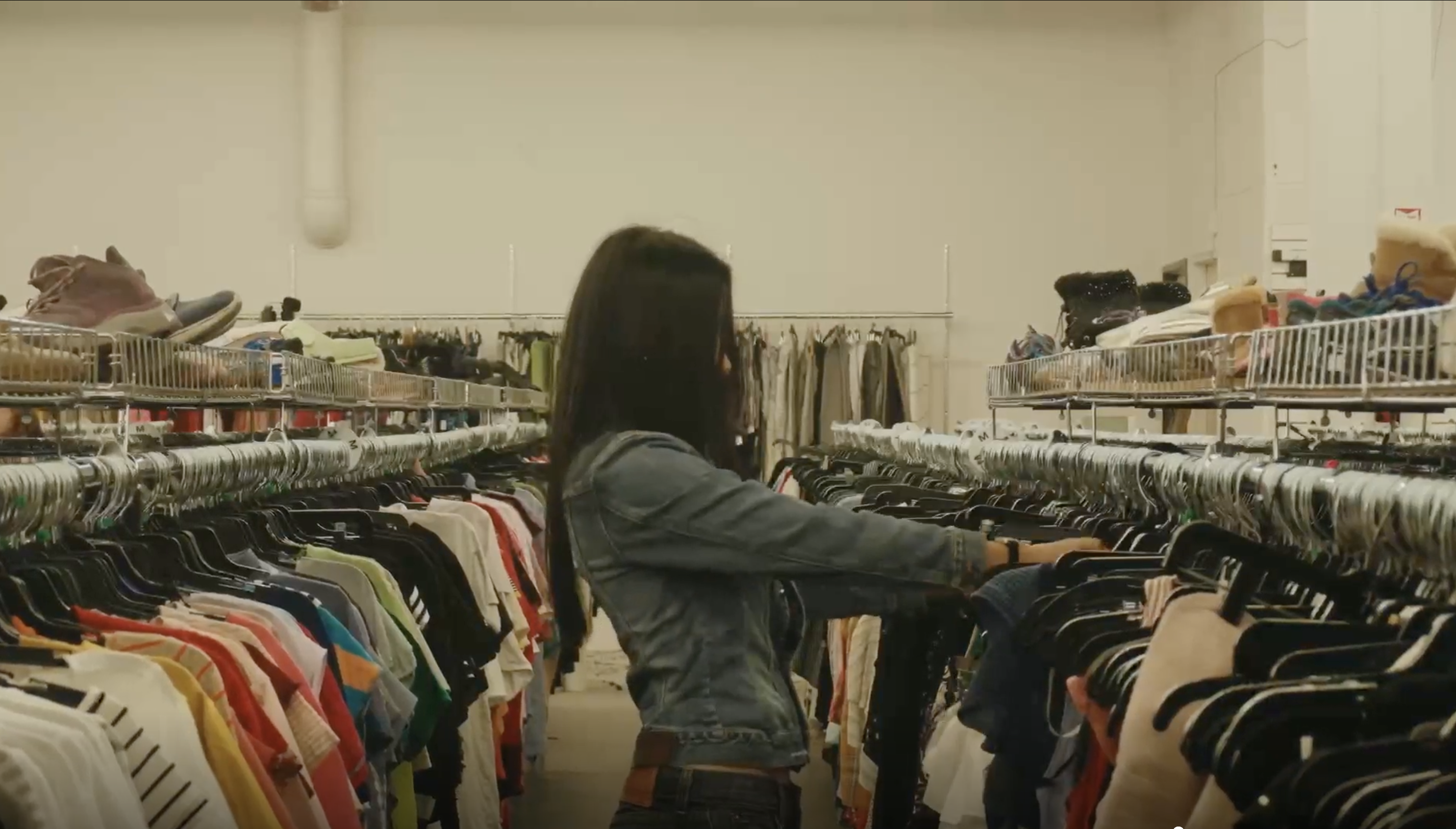 A woman in a denim jacket browses through racks of clothes in a store.