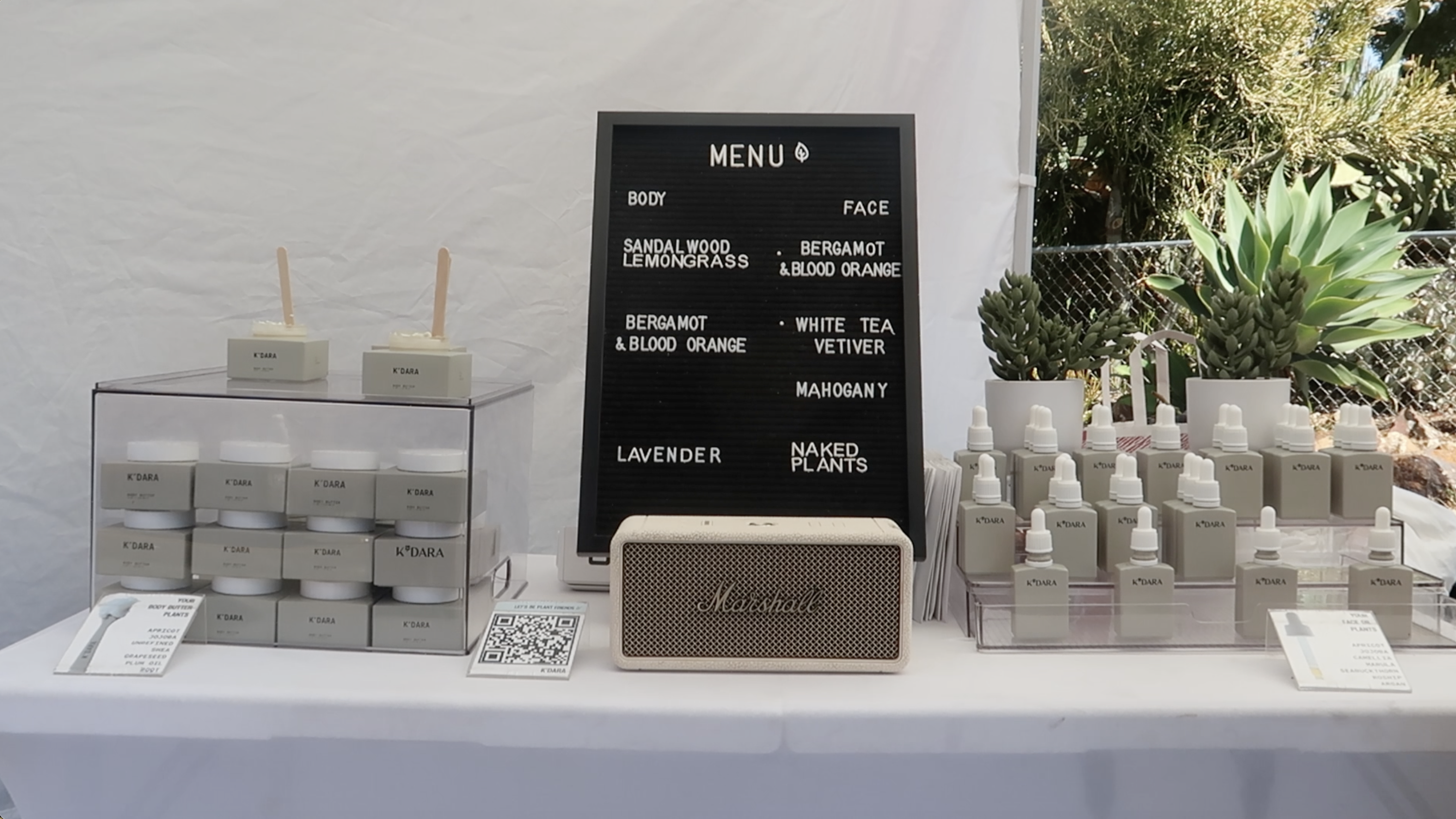 A display of K'DARA brand skincare products, a menu board, and a speaker on a white table.