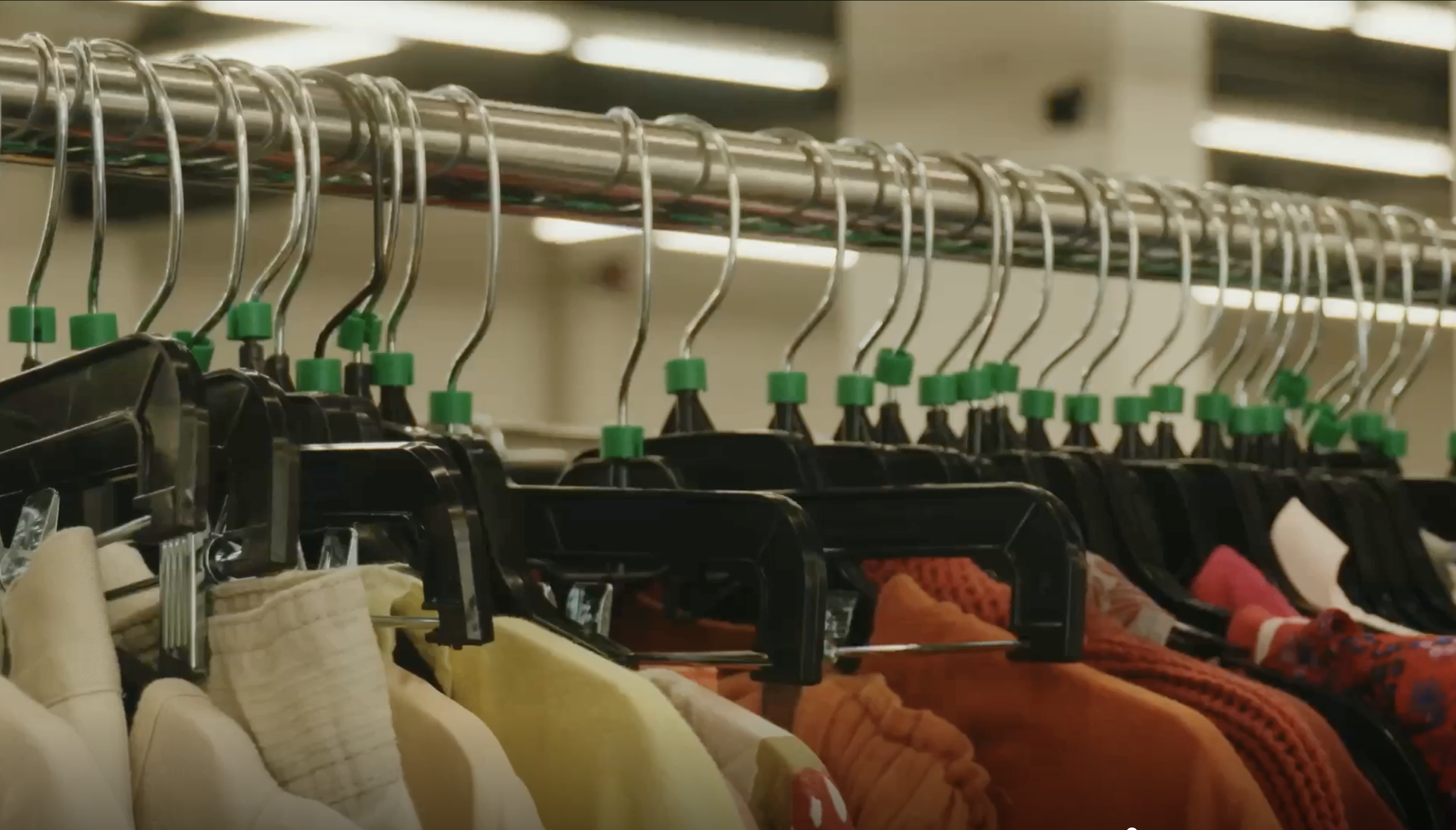 A close-up of various clothes hanging on black hangers with green markers on a metal rack.