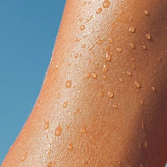 Close-up of wet skin with water droplets against a blue sky.