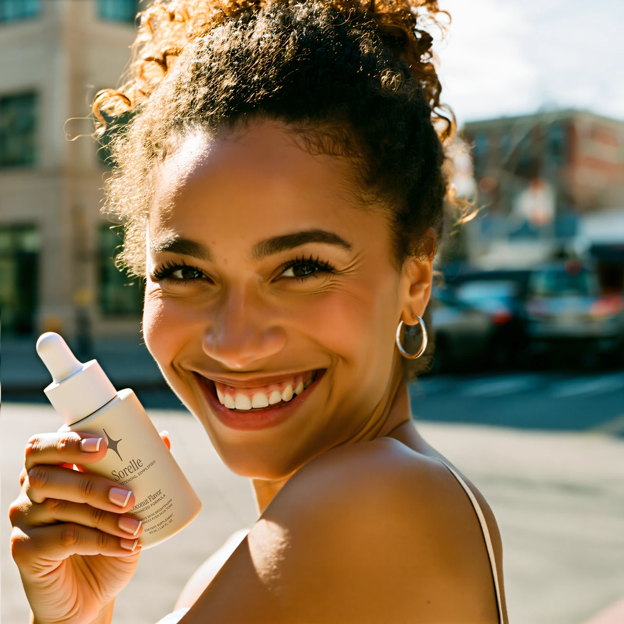 Smiling person holding a skincare product outdoors.
