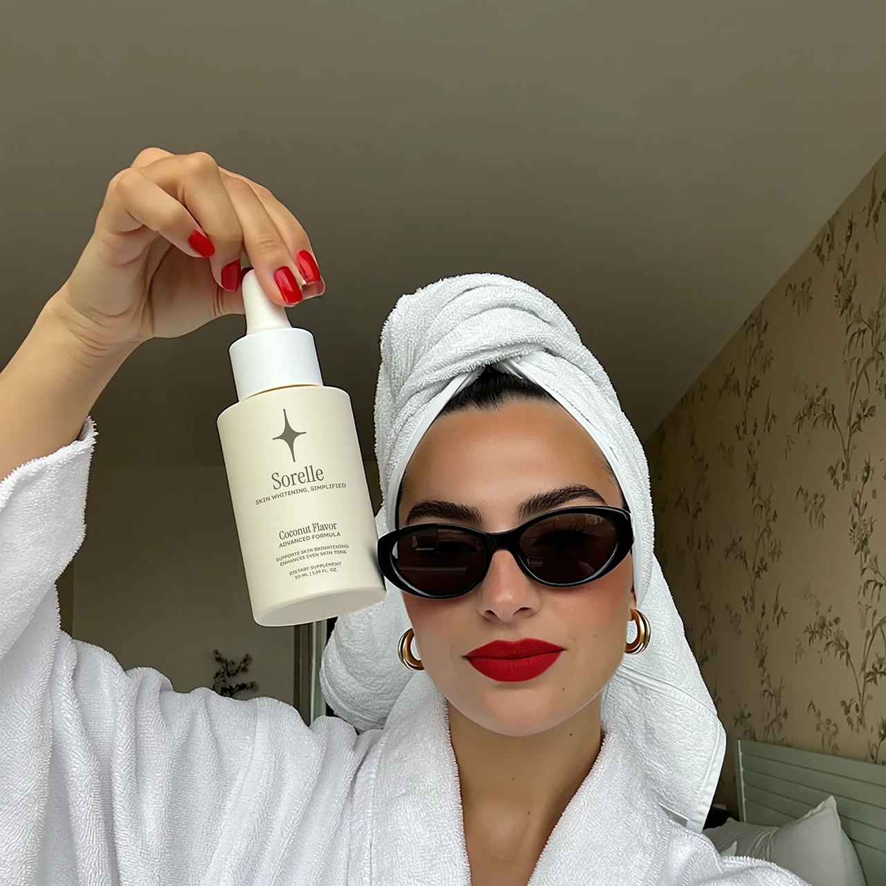 Person in a robe and sunglasses holding a skincare product bottle.