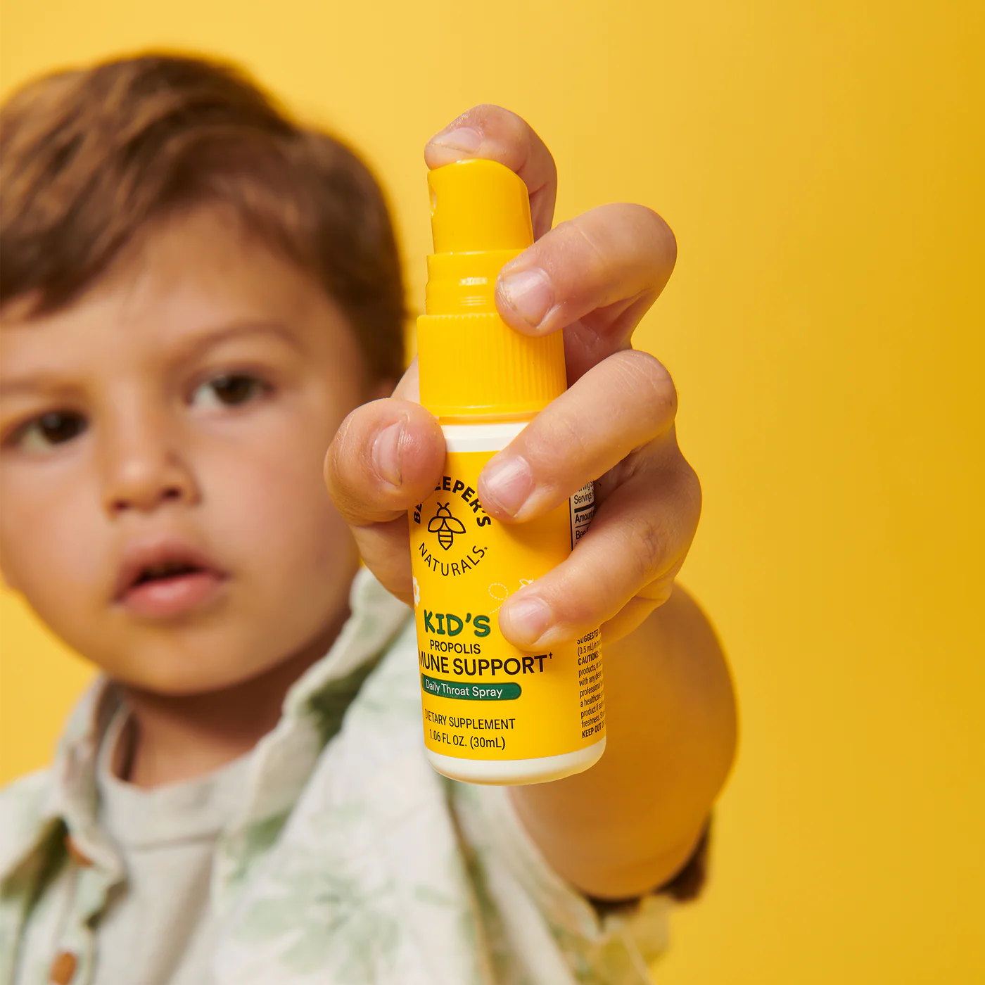 Child holding a yellow bottle against a yellow background.