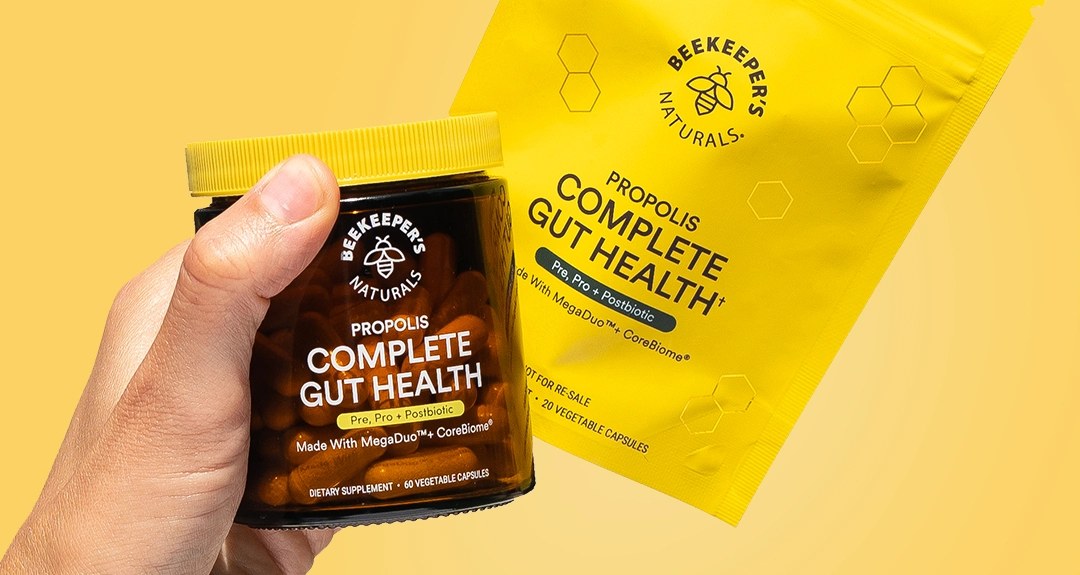 Hand holding jar and pouch of Beekeeper's Naturals Complete Gut Health supplements.
