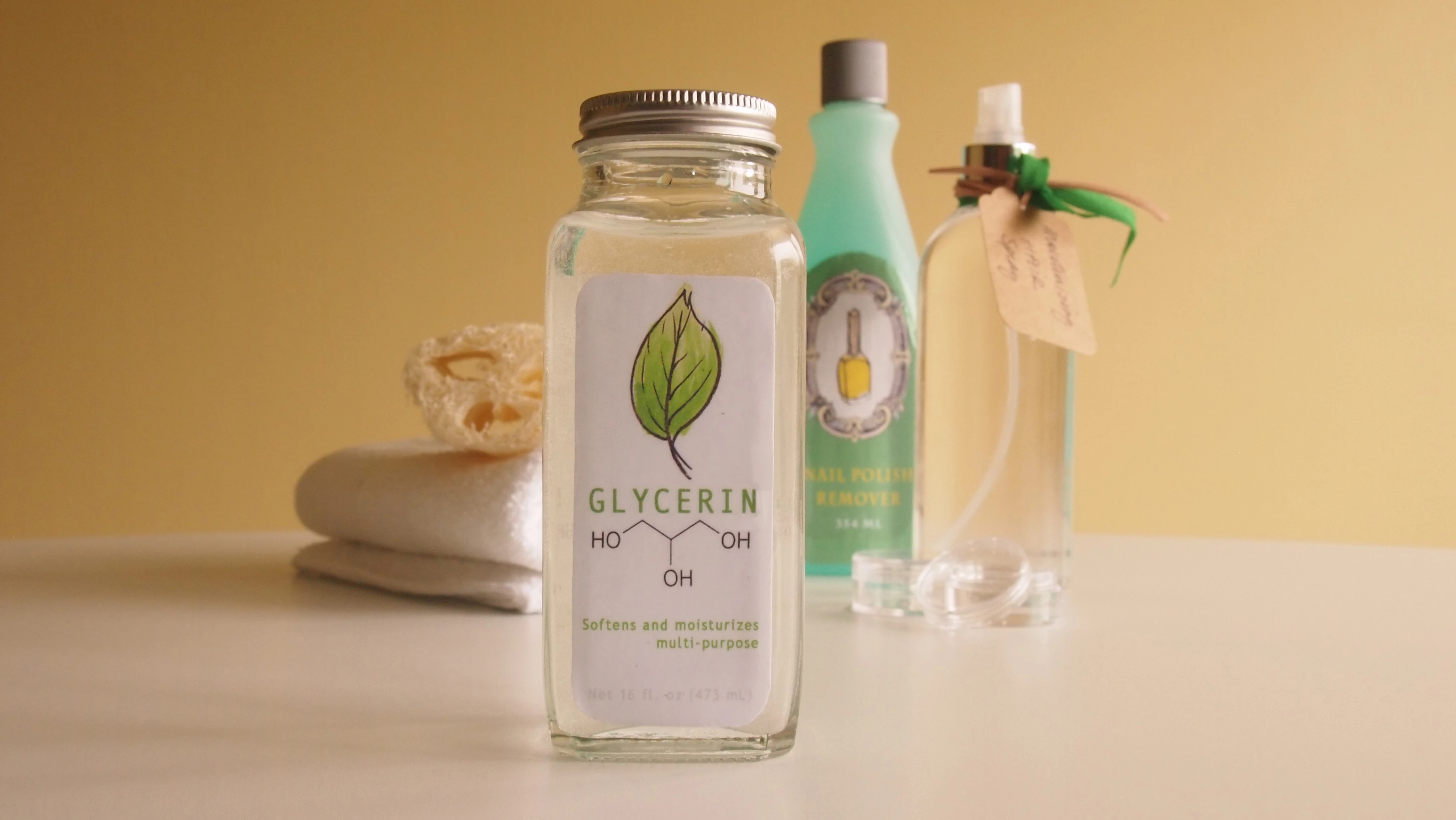 Glass bottle of glycerin with a leaf label, next to other bottles and a towel.