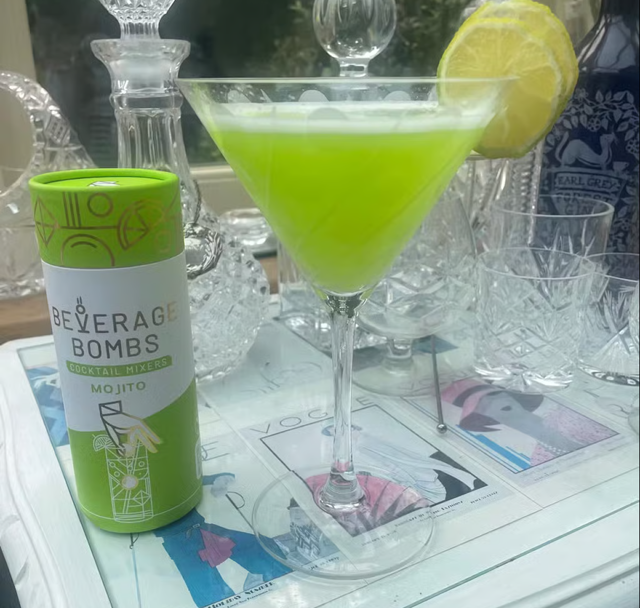 A green mojito in a martini glass next to a tube of Beverage Bombs cocktail mixers.