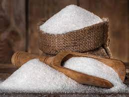 A burlap sack and wooden scoop filled with white sugar on a wooden surface.