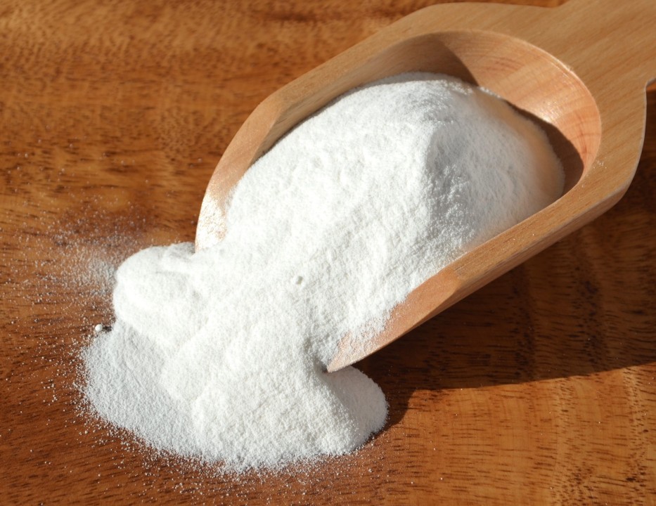 Wooden scoop with white powder on a wooden surface.