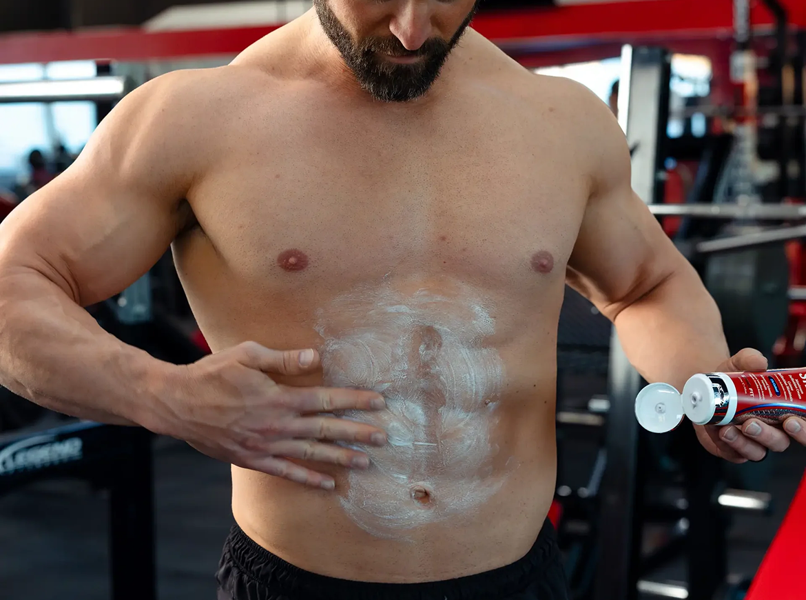A person holding a white container of STEELFIT Creatine Monohydrate supplement against their torso.