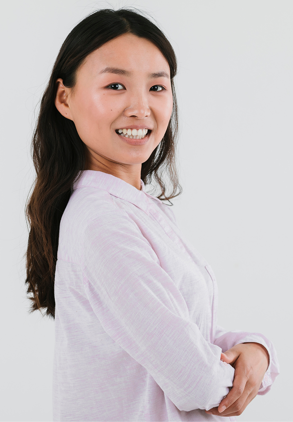 Person smiling, wearing a light pink button-up shirt, arms crossed.
