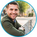Man smiling outdoors, leaning on a railing.