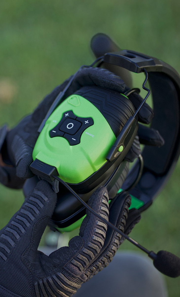 Person holding earmuffs with microphone and green control buttons.