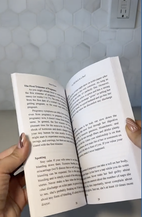 Person holding an open book with text about pregnancy in a brightly lit room.