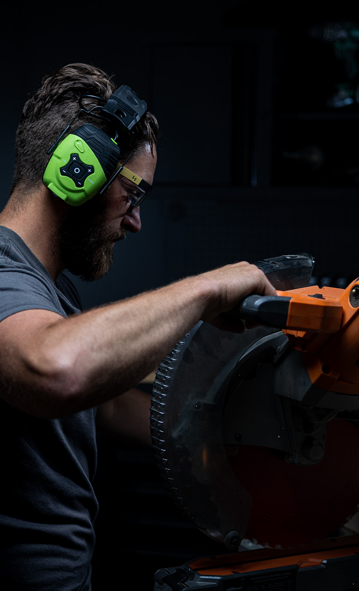 Man using a power saw, wearing protective earmuffs and safety glasses.