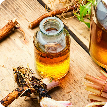 A small glass bottle of amber liquid sits on a wooden surface, surrounded by various plant roots and stems.