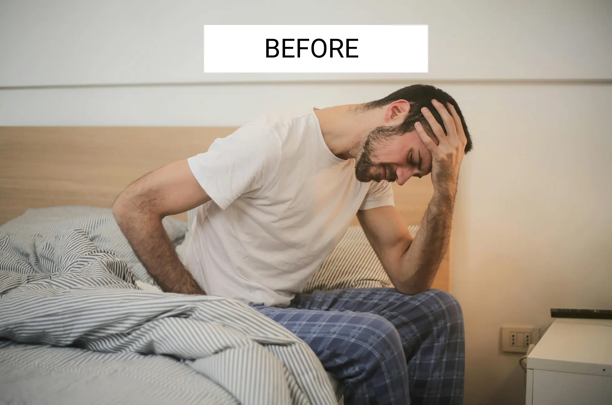 Man sitting on bed holding head, looking distressed.