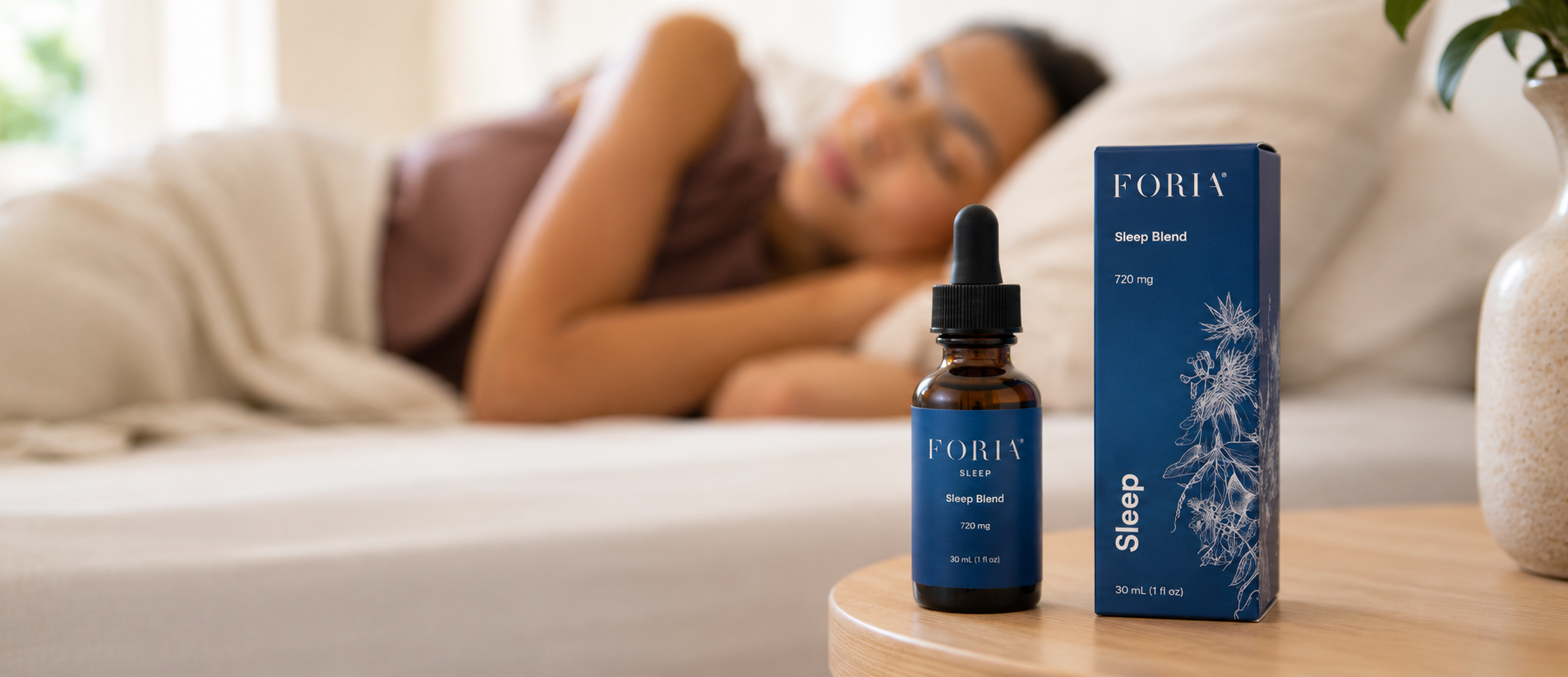 A bottle and box of Foria Sleep Blend sit on a nightstand with a person sleeping in the background.