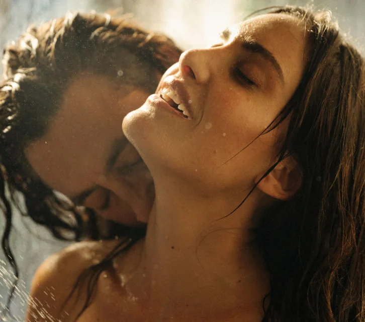 Two people embracing under water, eyes closed, with droplets on their skin.