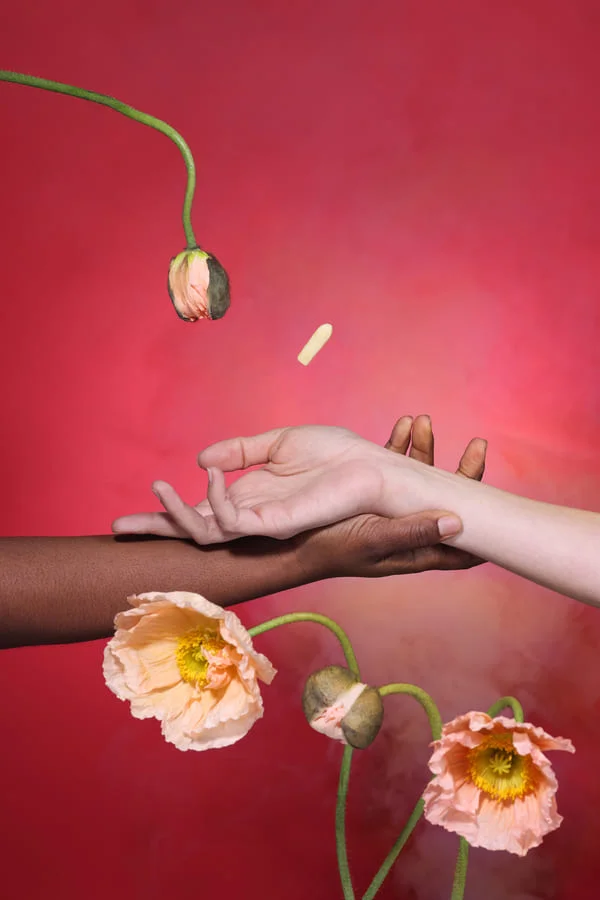 Hand reaching for brown dropper bottles on pink background with flowers.