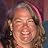 A close-up, slightly blurry headshot of a smiling woman with long, light-colored hair.