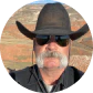 A man with a large white mustache wearing a cowboy hat and sunglasses outdoors.