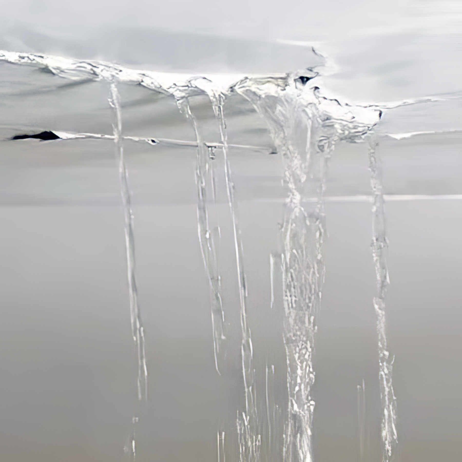 Close-up of water leaking in several streams from a damaged white ceiling.
