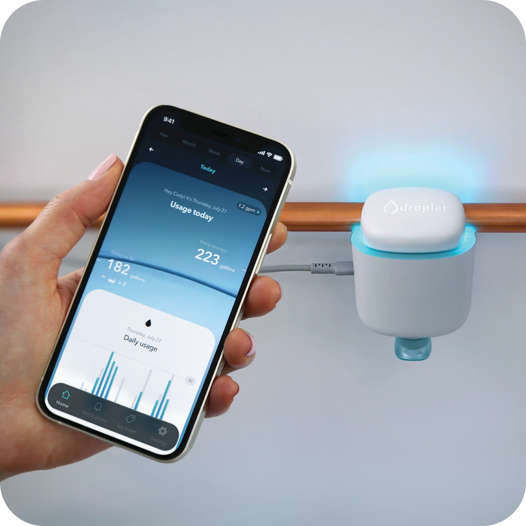 Hand holding smartphone displaying water usage app near smart water sensor.