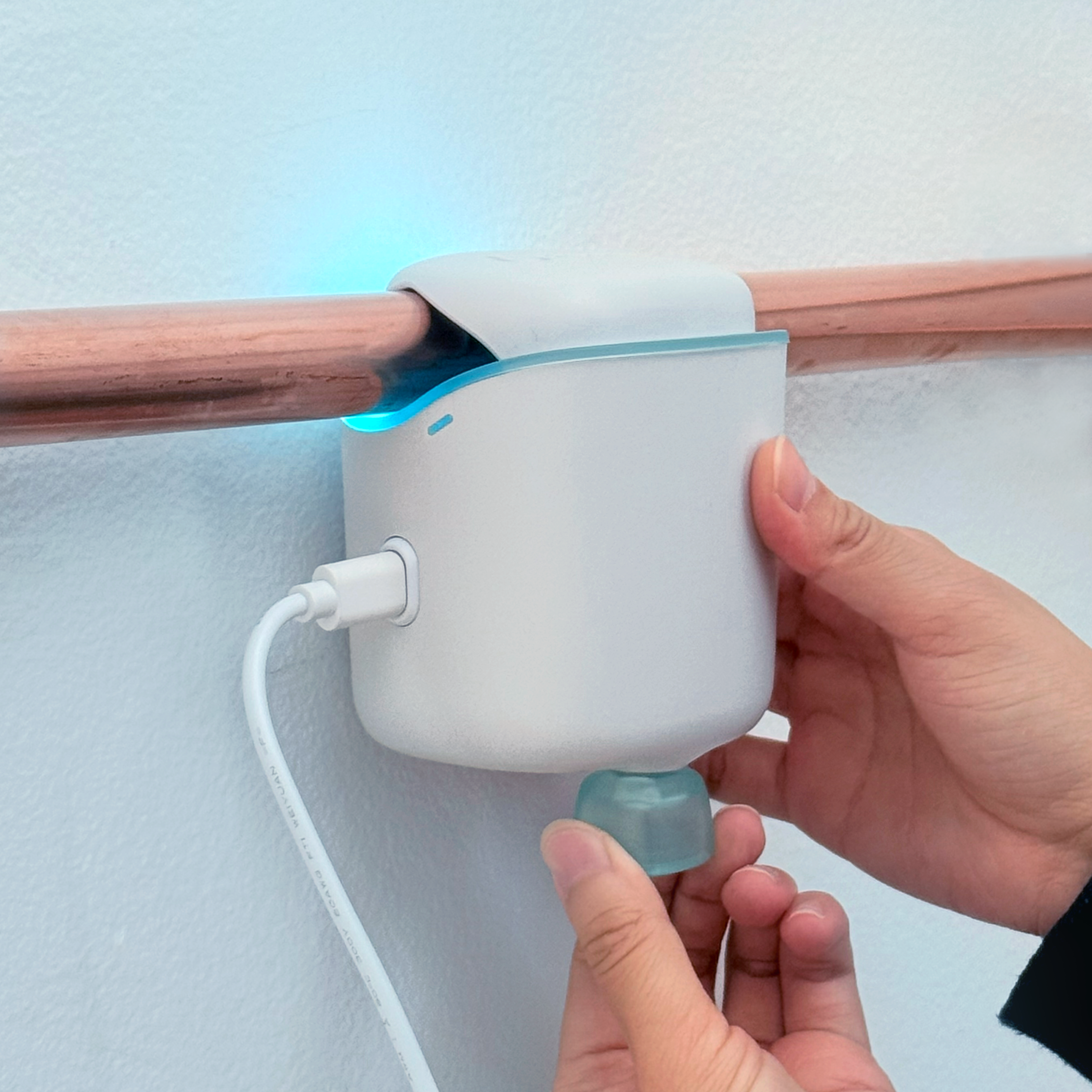 Hands adjusting a white device attached to a copper pipe on a wall.