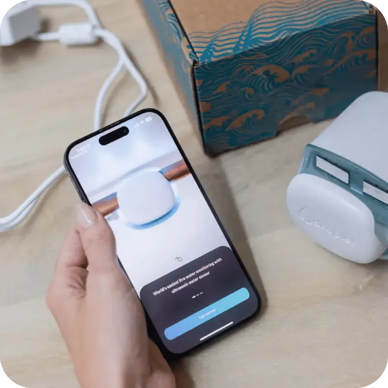 A person holds a smartphone showing the setup screen for a water monitoring device.