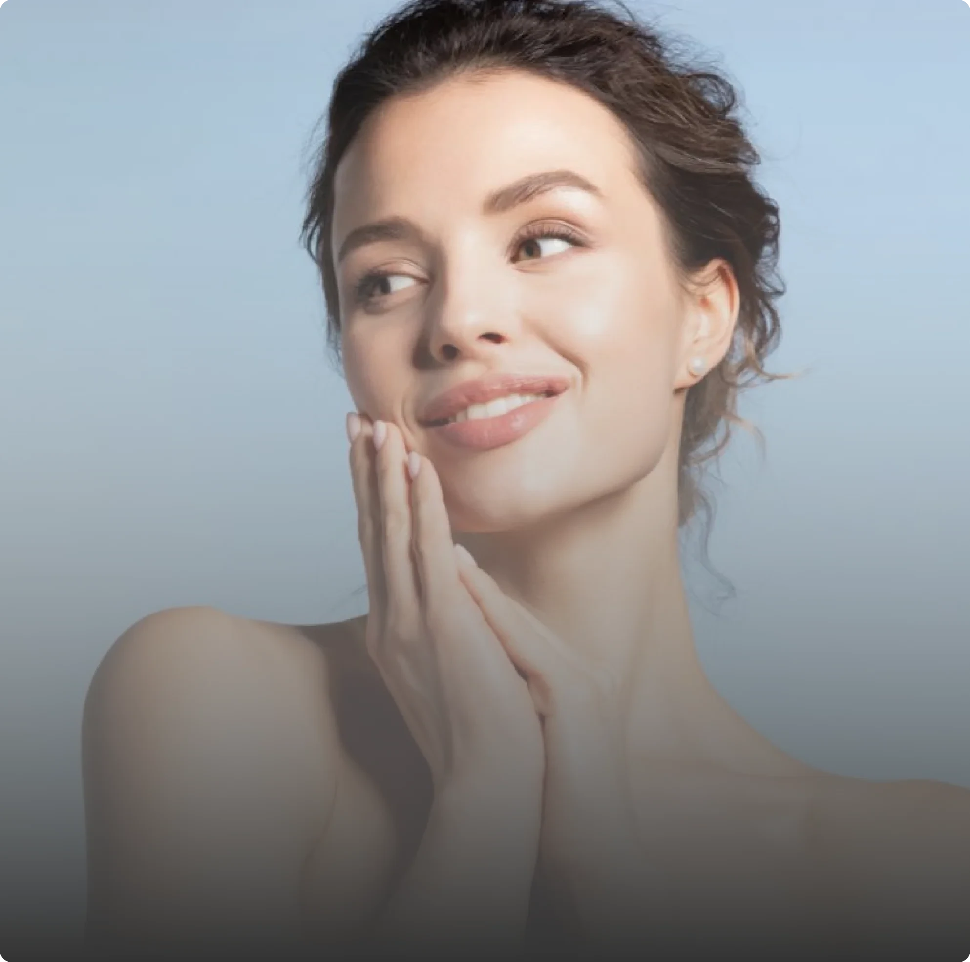 A smiling woman with her hair in an updo touches her face with both hands.