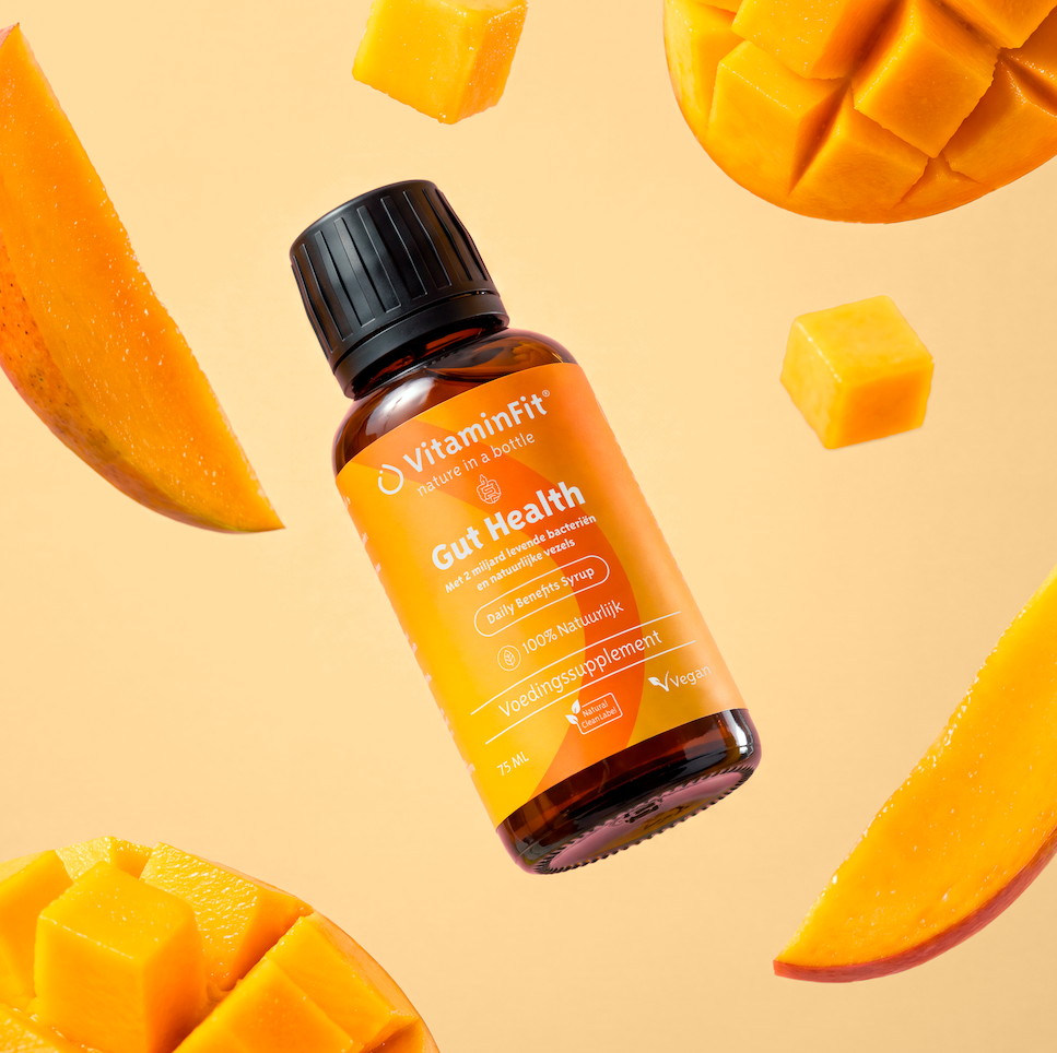 A bottle of VitaminFit Gut Health supplement is surrounded by fresh pieces of mango against a peach background.