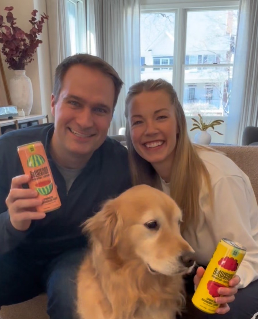 Two people smiling with a golden retriever and a can of beverage.