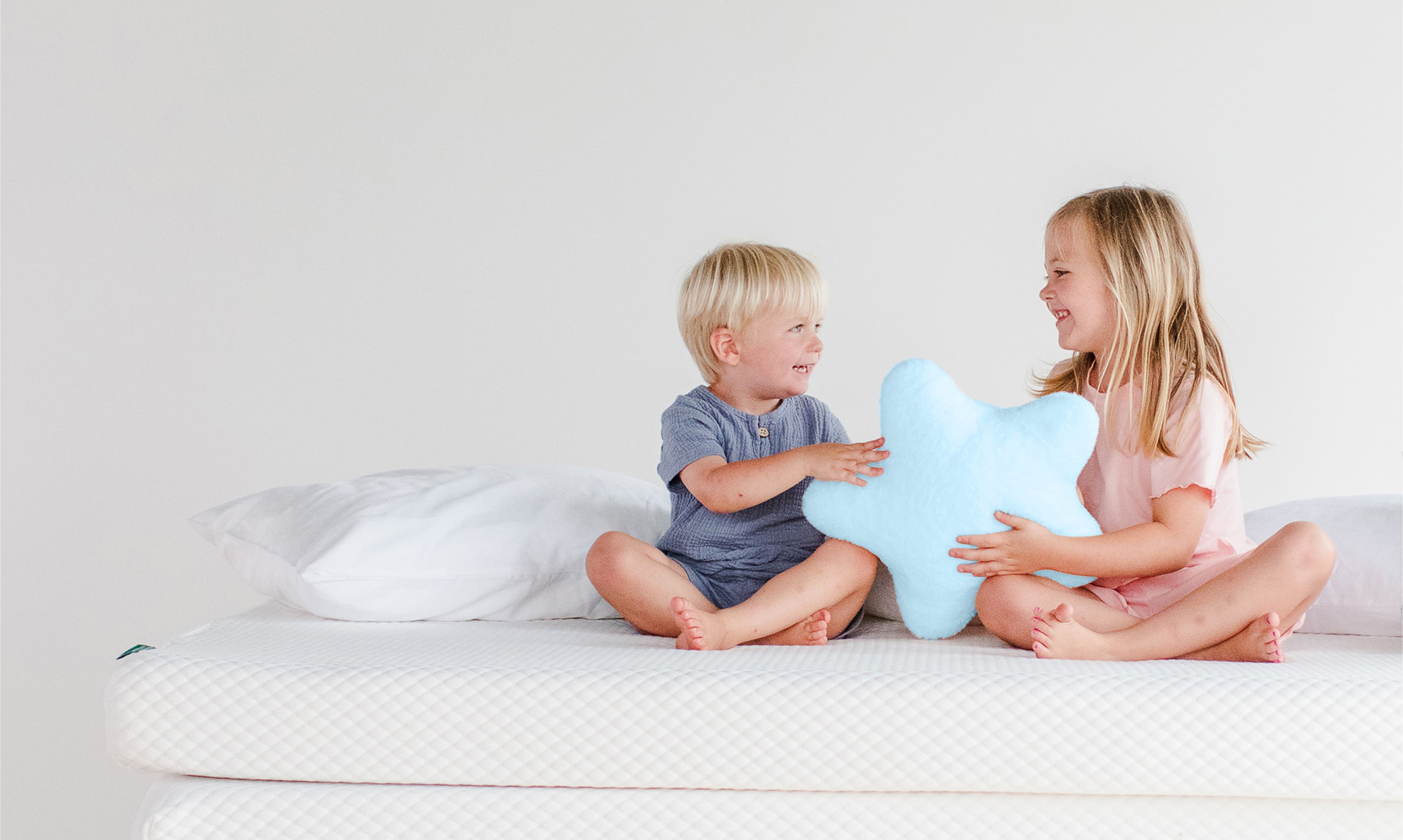 Two children sitting on stacked mattresses with pillows.