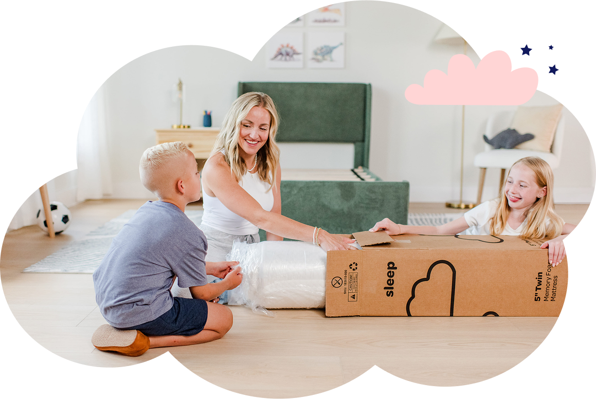 A woman unboxing a boxed mattress with a young boy and girl helping. The boy pulls on the mattress while the girl holds the box. 